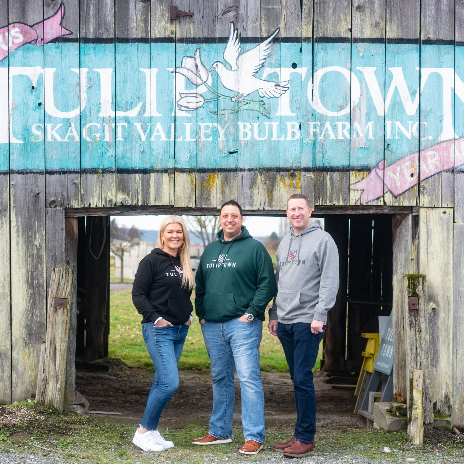 Tulip Town owners standing in front of the barn displaying the original Tulip Town logo, showcasing the farm’s legacy